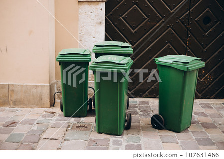 Public trashes on the side of the road. Plastic green wheeled recycling rubbish bins beside the road for rubbish collection. Ecology concept Public trashes on the side of the road. Plastic green wheeled recycling rubbish bins beside the road for rubbish collection. Ecology concept 107631466