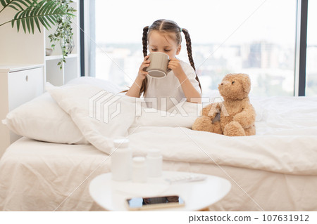 Tired kid taking sip of tea to easing sore throat in bed Tired kid taking sip of tea to easing sore throat in bed 107631912