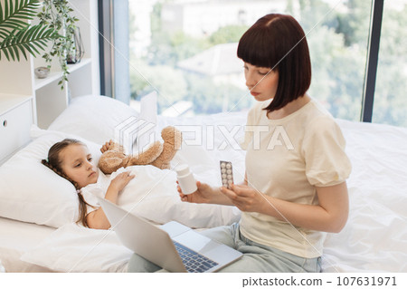 Mother using laptop for video chat with doctor for ill child Mother using laptop for video chat with doctor for ill child 107631971