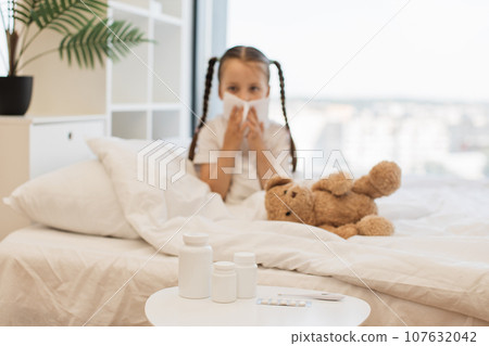 Sad ill girl sitting in bed and blowing nose into tissue 107632042