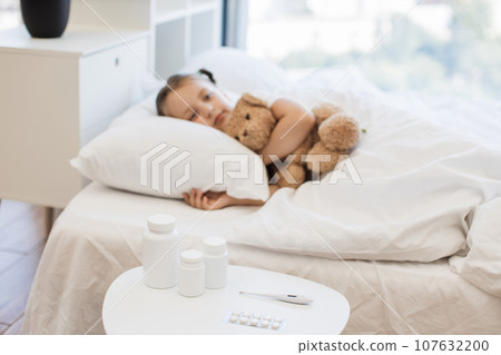 Little girl with virus resting on comfy bed with toy bear 107632200