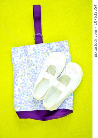 New white shoes and cute handmade purple mimosa flower pattern shoe bags on a yellow-green carpet, vertical 107632354
