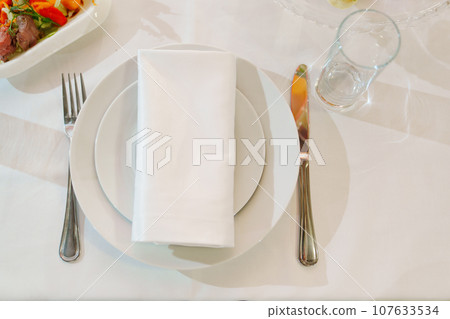 White round plate with serving napkin on table. White round plate with serving napkin on table. 107633534