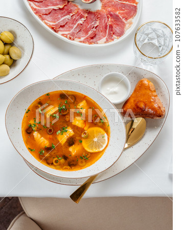 Solyanka soup with meat and olives garnished with a slice of lemon. Traditional Russian meat soup Solyanka in bowl on restaurant table. Top view or flat lay. Solyanka soup with meat and olives garnished with a slice of lemon. Traditional Russian meat soup Solyanka in bowl on restaurant table. Top view or flat lay. 107633582