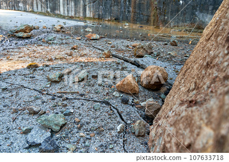 A huge rock fell from the mountains onto the road, destroying the asphalt and blocking half of the roadway 107633718