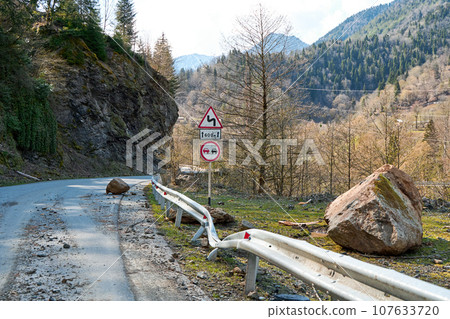 A huge rock fell from the mountains onto the road, destroying the asphalt and blocking half of the roadway A huge rock fell from the mountains onto the road, destroying the asphalt and blocking half of the roadway 107633720