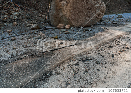 A huge rock fell from the mountains onto the road, destroying the asphalt and blocking half of the roadway A huge rock fell from the mountains onto the road, destroying the asphalt and blocking half of the roadway 107633721