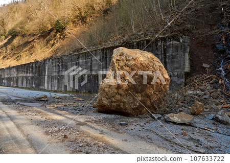 A huge rock fell from the mountains onto the road, destroying the asphalt and blocking half of the roadway A huge rock fell from the mountains onto the road, destroying the asphalt and blocking half of the roadway 107633722