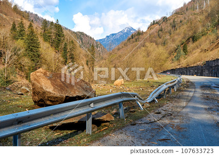 A huge rock fell from the mountains onto the road, destroying the asphalt and blocking half of the roadway A huge rock fell from the mountains onto the road, destroying the asphalt and blocking half of the roadway 107633723