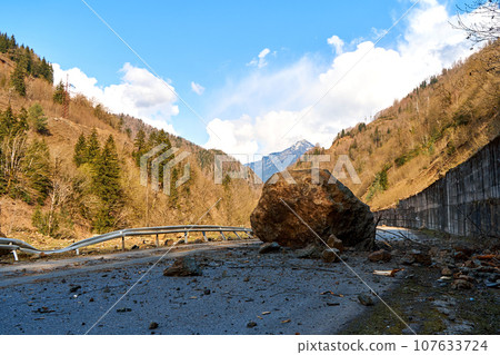 A huge rock fell from the mountains onto the road, destroying the asphalt and blocking half of the roadway 107633724