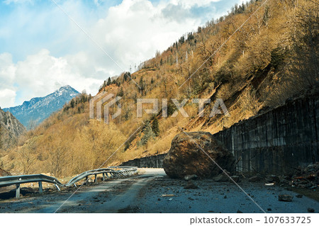 A huge rock fell from the mountains onto the road, destroying the asphalt and blocking half of the roadway A huge rock fell from the mountains onto the road, destroying the asphalt and blocking half of the roadway 107633725