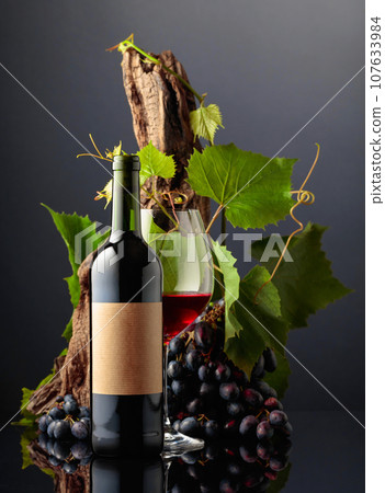 Glass and bottle of red wine with blue grapes and vine branches. Glass and bottle of red wine with blue grapes and vine branches. 107633984