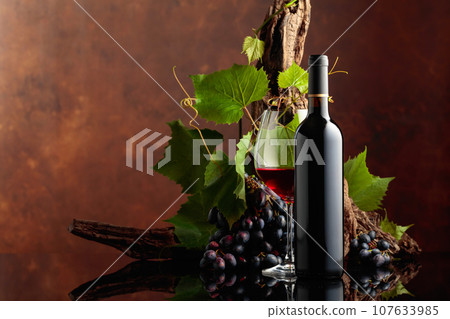 Glass and bottle of red wine with blue grapes and vine branches. Glass and bottle of red wine with blue grapes and vine branches. 107633985
