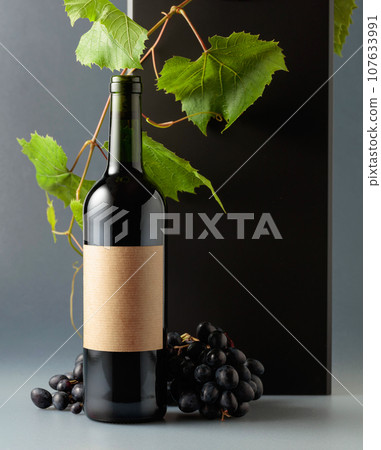 Bottle of red wine with blue grapes and vine branches. 107633991