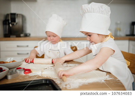 Adorable kids in chef hats and aprons rolling out pastry dough Adorable kids in chef hats and aprons rolling out pastry dough 107634083