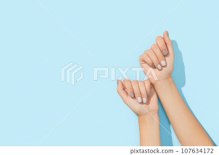 Womans hands with gray nail design on blue background Womans hands with gray nail design on blue background 107634172