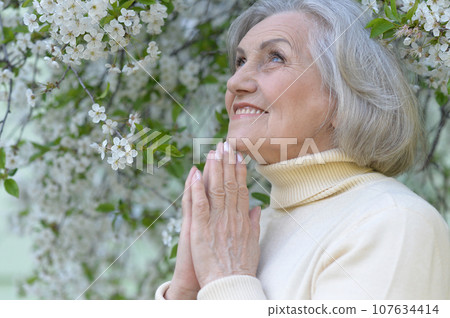 Close-up portrait of smiling elderly woman posing in summer park Close-up portrait of smiling elderly woman posing in summer park 107634414