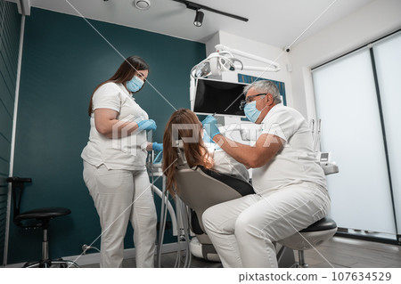 The patient receives comprehensive professional care from a dental expert. A dentist and a dental assistant work intently on the health and beauty of the patient's smile. The patient receives comprehensive professional care from a dental expert. A dentist and a dental assistant work intently on the health and beauty of the patient's smile. 107634529