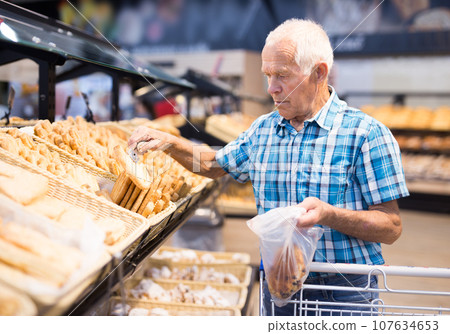 Old age senor examines bakery products in the grocery section of the supermarket 107634653