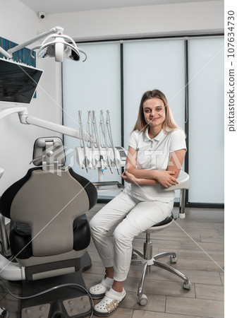 A dentist poses against the background of a dental chair, demonstrating professionalism and confidence. A dentist straightens teeth using modern technologies. A dentist poses against the background of a dental chair, demonstrating professionalism and confidence. A dentist straightens teeth using modern technologies. 107634730