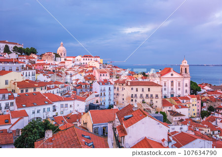 View of Lisbon famous view from Miradouro de Santa Luzia tourist viewpoint over Alfama old city district on sunset with dramatic overcast sky. Lisbon, Portugal. 107634790