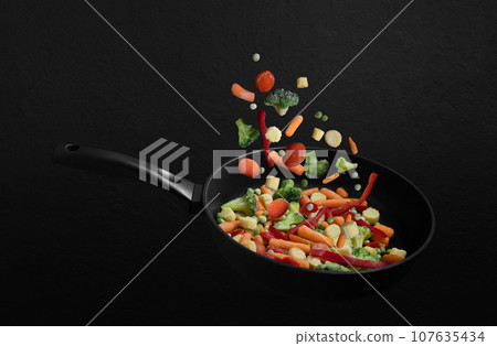 Falling frozen vegetables in a frying pan on black background. Vegetable mix flying down. Healthy natural food. 107635434