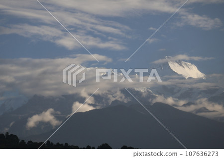 The snow-covered Himalayan mountain scenery glimpsed between the blue sky and the clouds illuminated by the morning light. 107636273