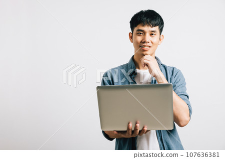 A closeup portrait of a thoughtful Asian man, hand on chin, holding a laptop, pondering questions and looking away. Studio shot isolated on white, where success is born from deep thinking. A closeup portrait of a thoughtful Asian man, hand on chin, holding a laptop, pondering questions and looking away. Studio shot isolated on white, where success is born from deep thinking. 107636381
