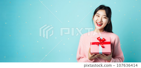 Happy carefree asian woman having fun with gift in hands on a blue minimal banner 107636414