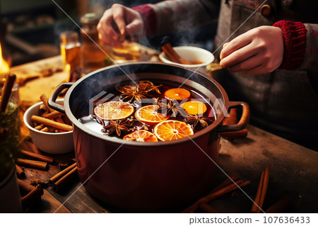 Woman cooking traditional mulled wine in pot with orange slices and spices close-up 107636433