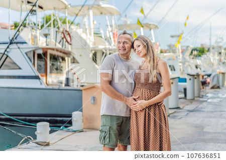 A happy, mature couple over 40, enjoying a leisurely walk on the waterfront, their joy evident as they embrace the journey of pregnancy later in life A happy, mature couple over 40, enjoying a leisurely walk on the waterfront, their joy evident as they embrace the journey of pregnancy later in life 107636851