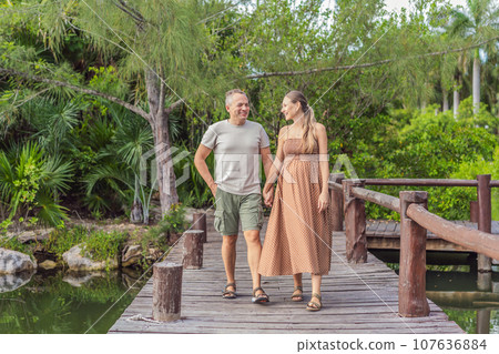 A happy, mature couple over 40, enjoying a leisurely walk in a park, their joy evident as they embrace the journey of pregnancy later in life 107636884