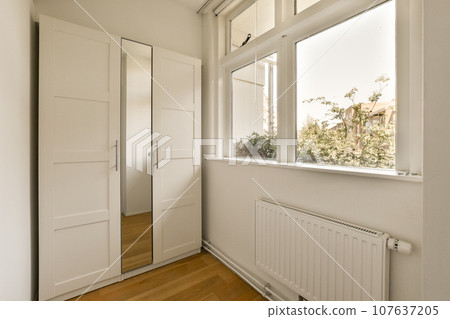 a room with white walls and wood flooring, there is a large window looking out to the garden outside a room with white walls and wood flooring, there is a large window looking out to the garden outside 107637205