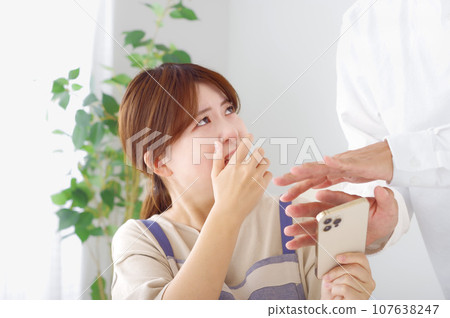 A woman makes a complicated expression when looking at a man's smartphone 107638247