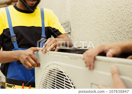 Trained engineer and certified technician opening up old faulty hvac system to replace it with new performant outside air conditioner after draining refrigerant and replacing ductwork 107638847