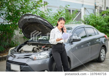 female motorist is calling an insurance or recovery service officer for assistance related to a car accident. 107640716