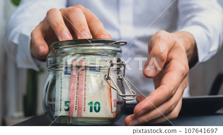 Euro Banknote Saving Money In Glass Jar. Unrecognizable man Moderate Consumption on calculator And Economy Collecting Money Tips Business Finance Euro Banknote Saving Money In Glass Jar. Unrecognizable man Moderate Consumption on calculator And Economy Collecting Money Tips Business Finance 107641697