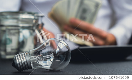 Electric light bulb. Man hands counting expenses bills on electricity banknotes of dollar cash accounting on calculator. Close up of hands unrecognizable Businessman. High prices for energy. Save up 107641699