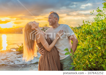 A happy, mature couple over 40, enjoying a leisurely walk on the waterfront On the Sunset, their joy evident as they embrace the journey of pregnancy later in life 107642252