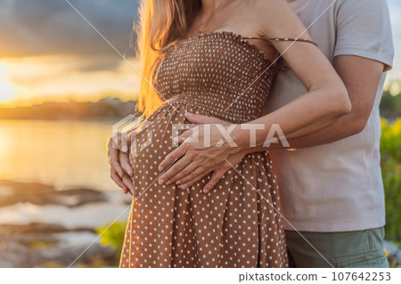 A happy, mature couple over 40, enjoying a leisurely walk on the waterfront On the Sunset, their joy evident as they embrace the journey of pregnancy later in life A happy, mature couple over 40, enjoying a leisurely walk on the waterfront On the Sunset, their joy evident as they embrace the journey of pregnancy later in life 107642253
