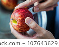 woman hand is cleaning red apple in bucket of water, closed up shot 107643629