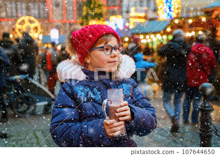 Little cute preschool girl drinking hot children punch or chocolate on German Christmas market. Happy child on traditional family market in Germany, Laughing kid in colorful winter clothes 107644650