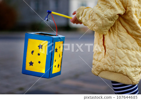 Closeup of little preschool kid girl holding selfmade traditional lanterns with candle for St. Martin procession. child happy about family parade in kindergarten. German tradition Martinsumzug Closeup of little preschool kid girl holding selfmade traditional lanterns with candle for St. Martin procession. child happy about family parade in kindergarten. German tradition Martinsumzug 107644685