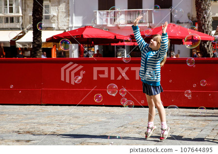 little girl playing on the street with blowing soap bubbles. Happy child in the city. little girl playing on the street with blowing soap bubbles. Happy child in the city. 107644895