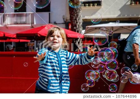 little girl playing on the street with blowing soap bubbles. Happy child in the city. little girl playing on the street with blowing soap bubbles. Happy child in the city. 107644896