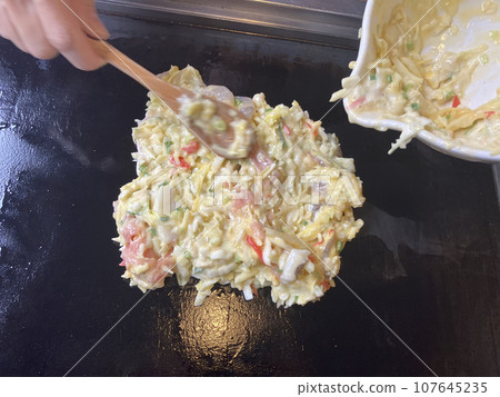 Putting okonomiyaki ingredients on the iron plate 107645235