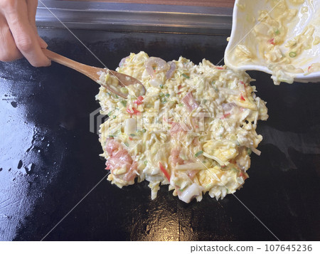 Putting okonomiyaki ingredients on the iron plate 107645236