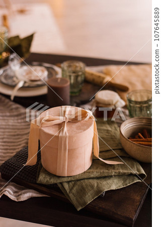 Stylish round powder-colored gift box with a ribbon and a bow stands on the festive table Stylish round powder-colored gift box with a ribbon and a bow stands on the festive table 107645889