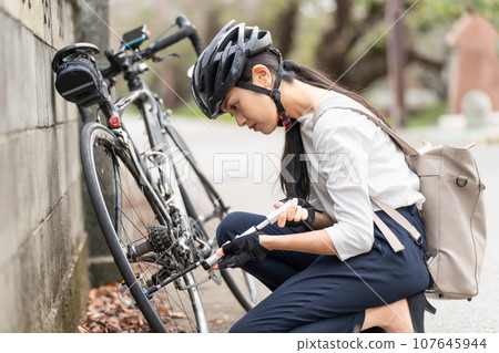 Young woman pumping air into her road bike with a portable pump 107645944