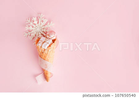 Ice Cream Cone with Christmas Decoration gift box, snowflake on pink pastel background. Minimal Christmas Concept. Flat Lay 107650540